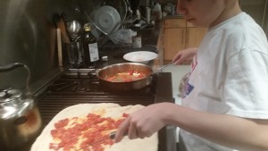 Max putting tomato sauce on pizza